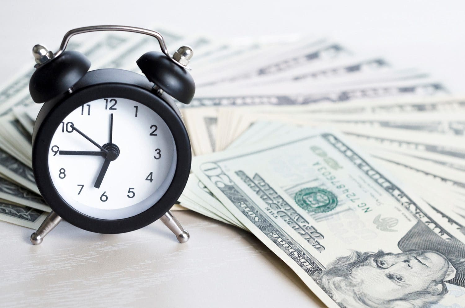 Black alarm clock resting on cash to represent time-sensitive investment strategies.