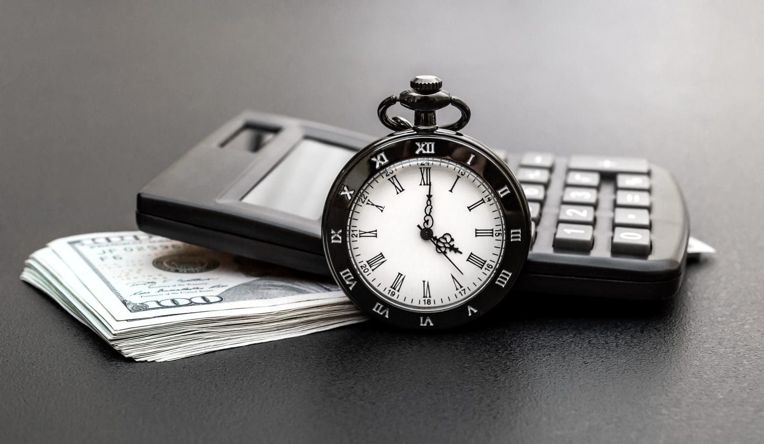 Financial tools including a pocket watch and a calculator on a stack of hundred-dollar bills.