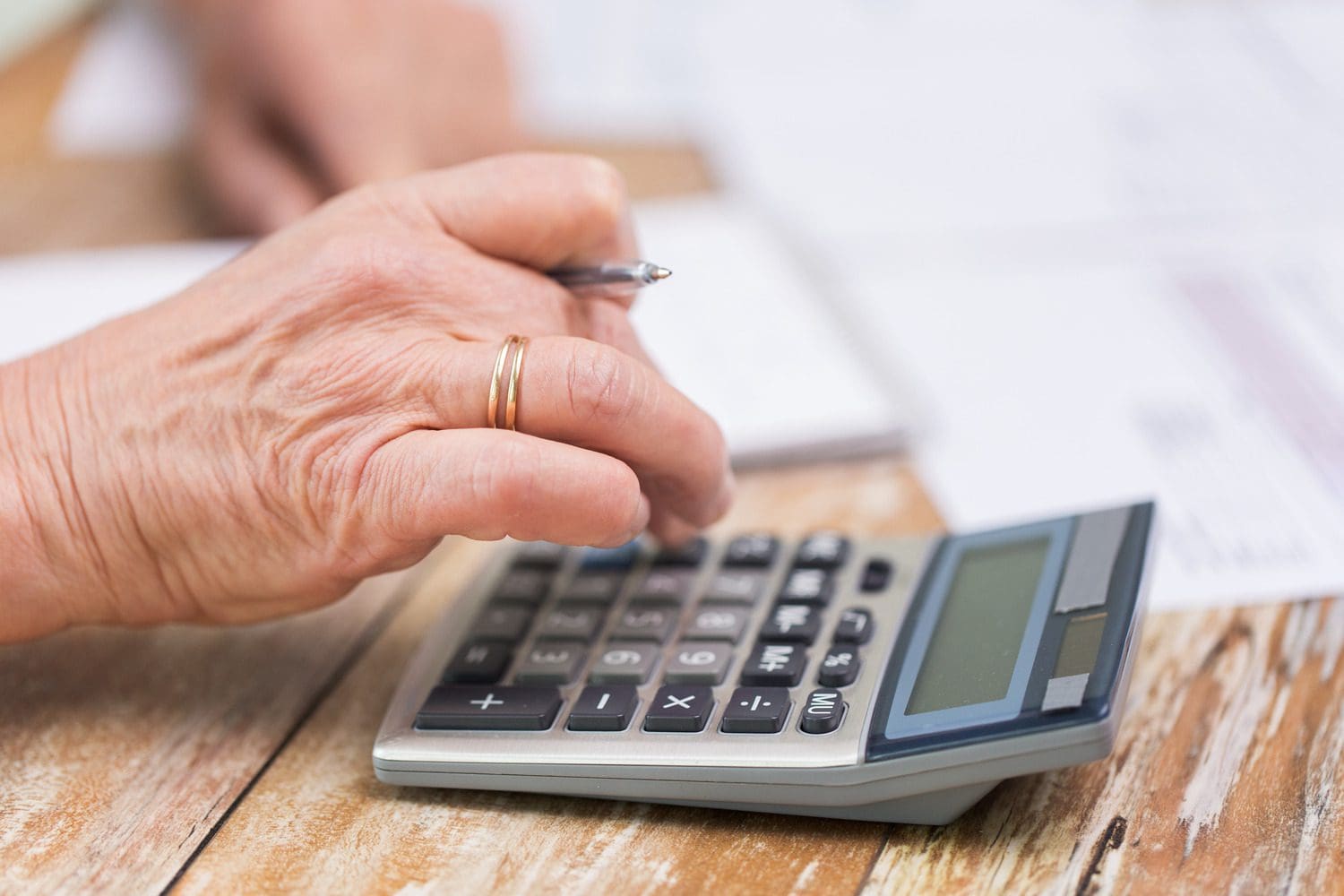 A senior investor using a calculator and reviewing paperwork for long-term care and retirement planning.