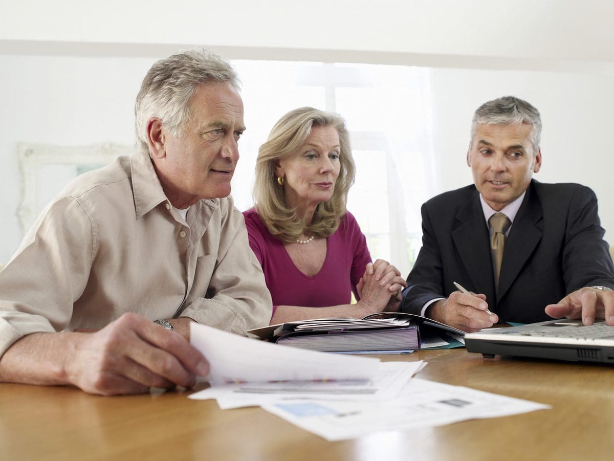 A mature couple reviewing financial documents and receiving guidance from a professional advisor.