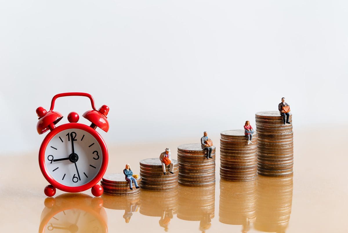 Conceptual image of retirement planning featuring miniature figures on coin stacks next to a red alarm clock