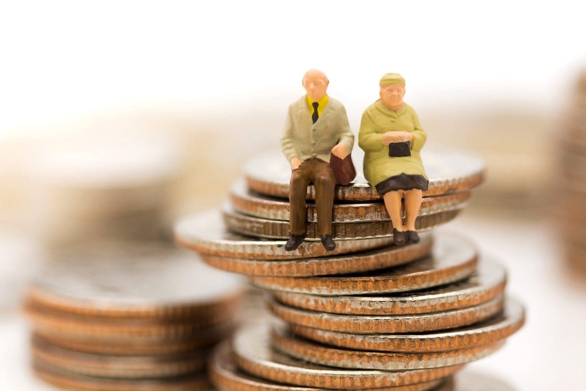 Concept of retirement savings illustrated with miniature elderly figures on coin stacks.