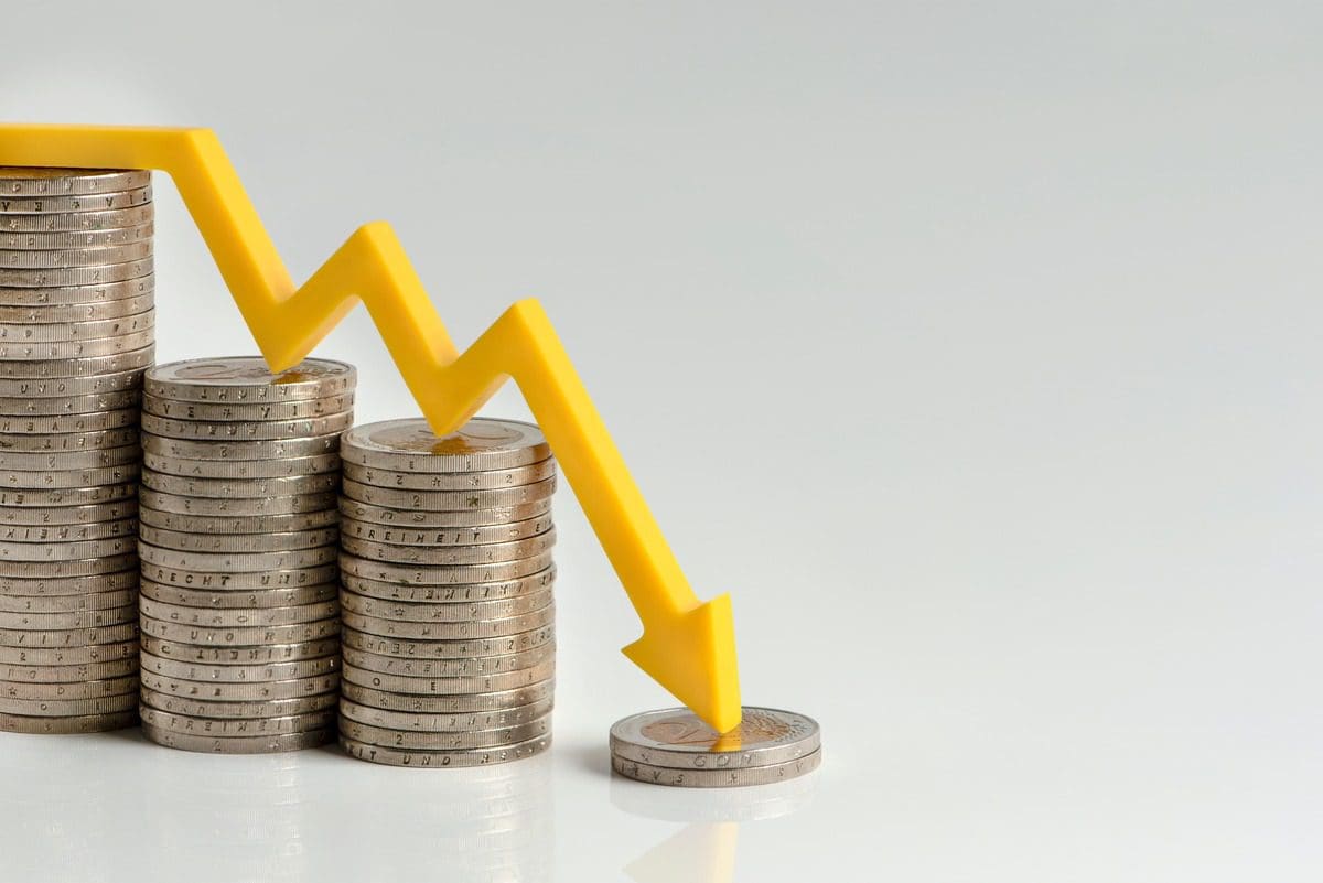 Conceptual illustration of a financial market decline with stacked coins and a descending arrow.