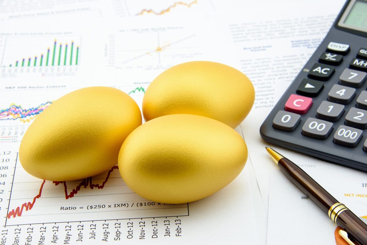 Three golden eggs placed on financial data charts representing investment growth and diversification.