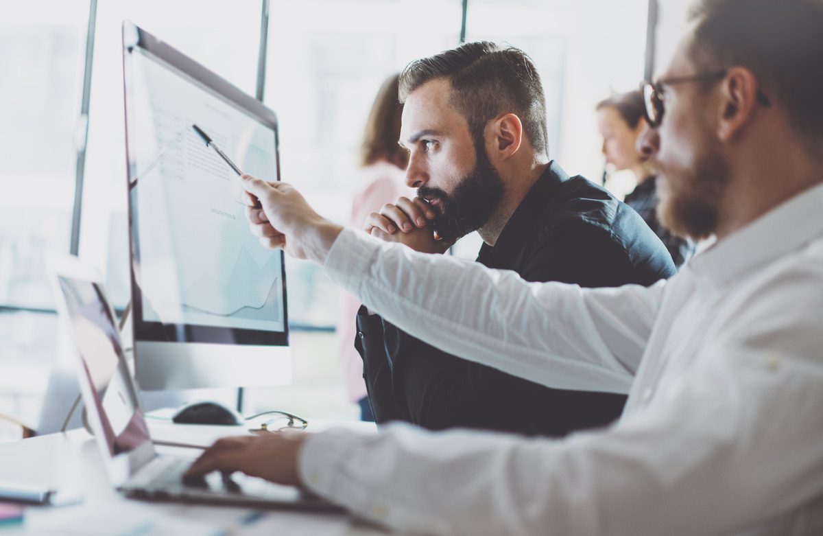 Two financial professionals analyzing stock market trends on a computer monitor