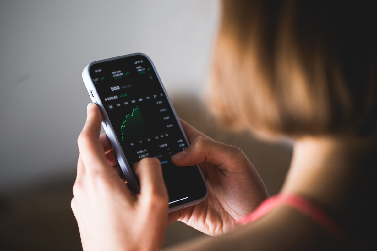 A person holding a smartphone displaying a stock market app interface for real-time analysis.
